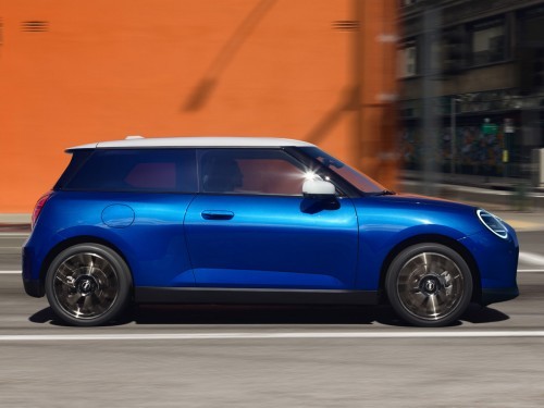 Blue MINI Cooper driving past an orange wall in an urban setting